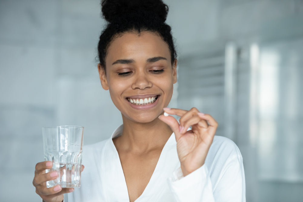 A woman stands in her bathroom while holding up a probiotic lozenge for bad breath.
