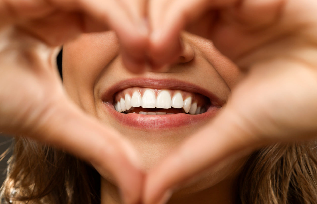An image of a woman smiling and making a heart shape gesture.
